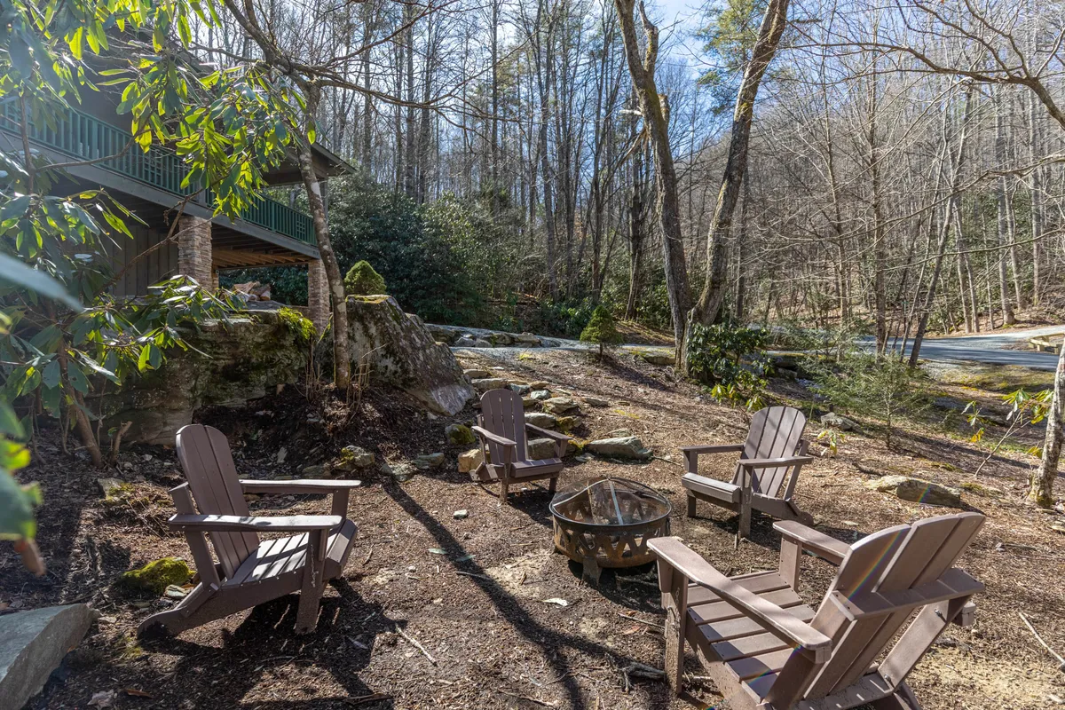 This image captures a cozy outdoor fire pit surrounded by adirondack chairs and natural rock formations, set beneath the trees. The scene evokes a sense of warmth and camaraderie, perfect for gathering under the stars and enjoying the seclusion of the forest.