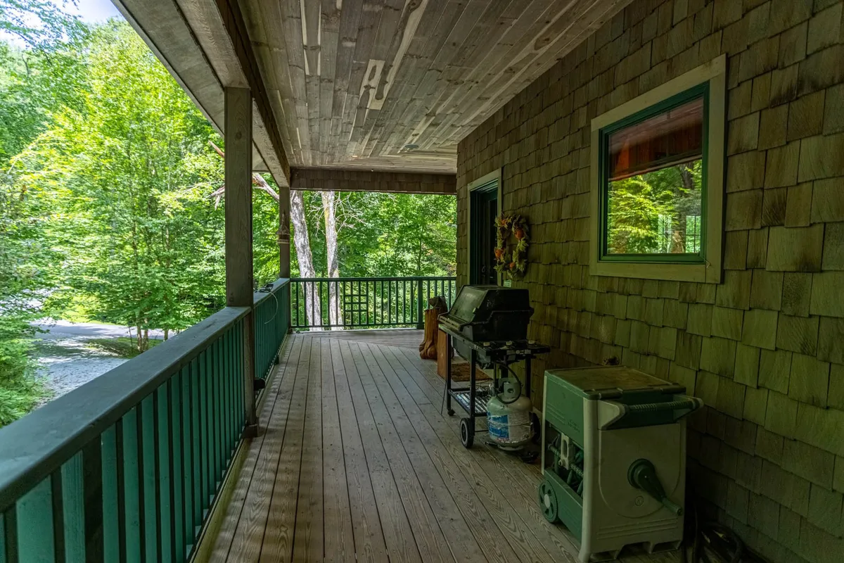 This exterior image features lush green foliage surrounding a welcoming wooden deck area, complete with a grill and wooden railing. A festive wreath adorns the front door, and the scene evokes relaxation and gatherings in a private natural setting.