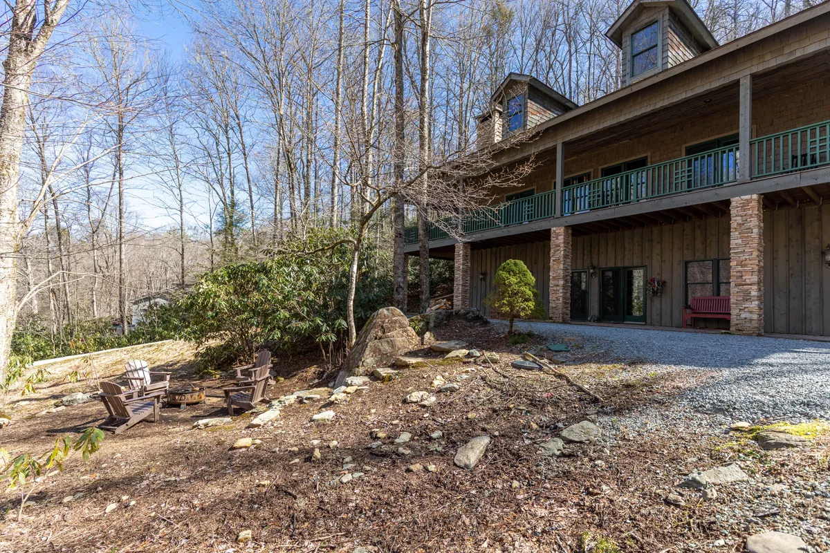 An outdoor wooden deck with a rock seating area nestled among surrounding trees. The setting feels peaceful and secluded, providing a space to enjoy nature, read, or gather near a fire pit as evening falls.