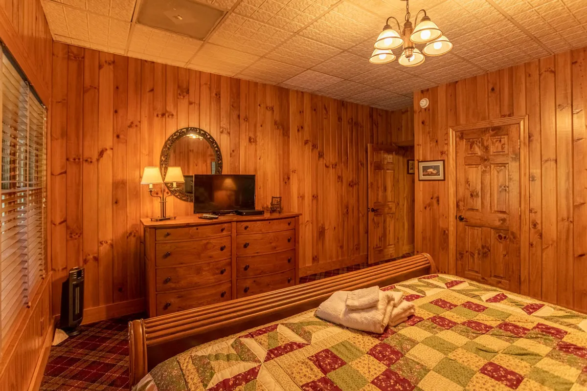 A second bedroom image with wooden walls, a quilted bedspread, television, and soft lighting from lamps. The ambiance is cozy and restful, ideal for unwinding in a private space.