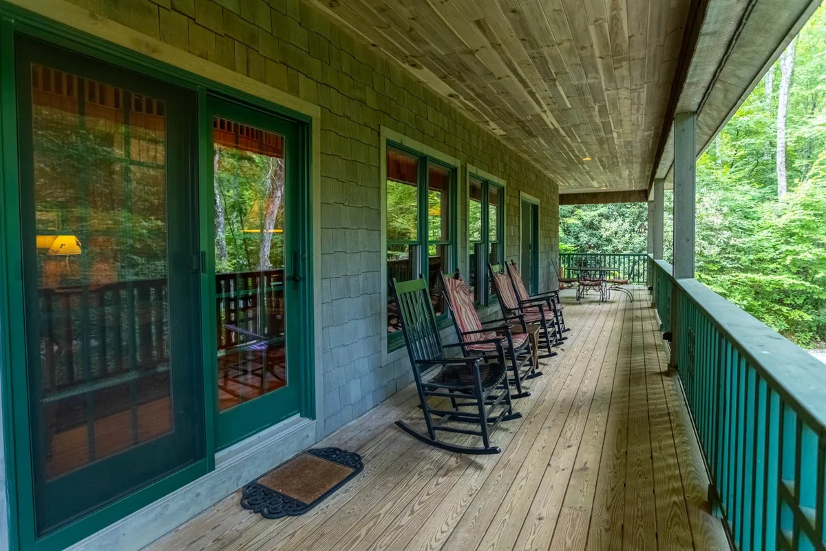A cozy wooden deck with green railings and rocking chairs, enhanced by large windows that blend the indoor and outdoor experience. The deck is ideal for savoring sunrises, enjoying casual social gatherings, or simply taking in the views after a day of adventure.