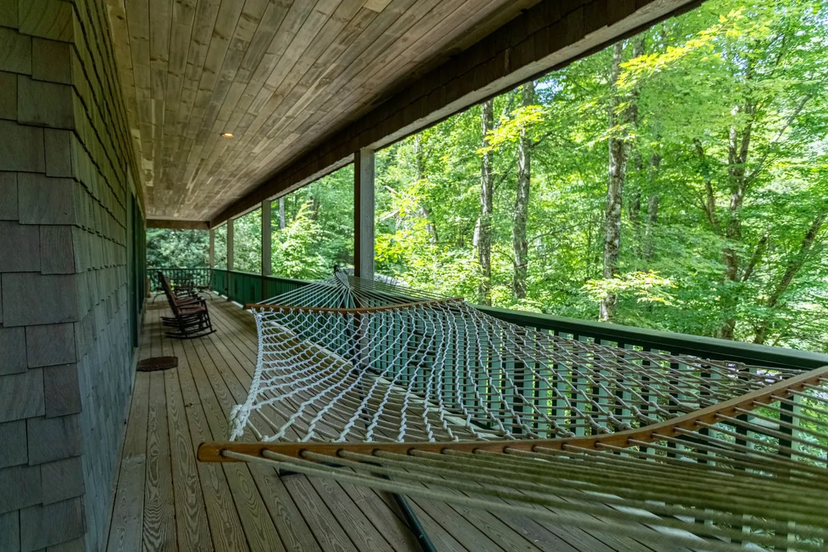 A hammock is hung between trees on a shaded deck, flanked by classic rocking chairs and surrounded by peaceful forest. The scene invites guests to immerse themselves in the tranquil setting, ideal for quiet reflection or evening stargazing.