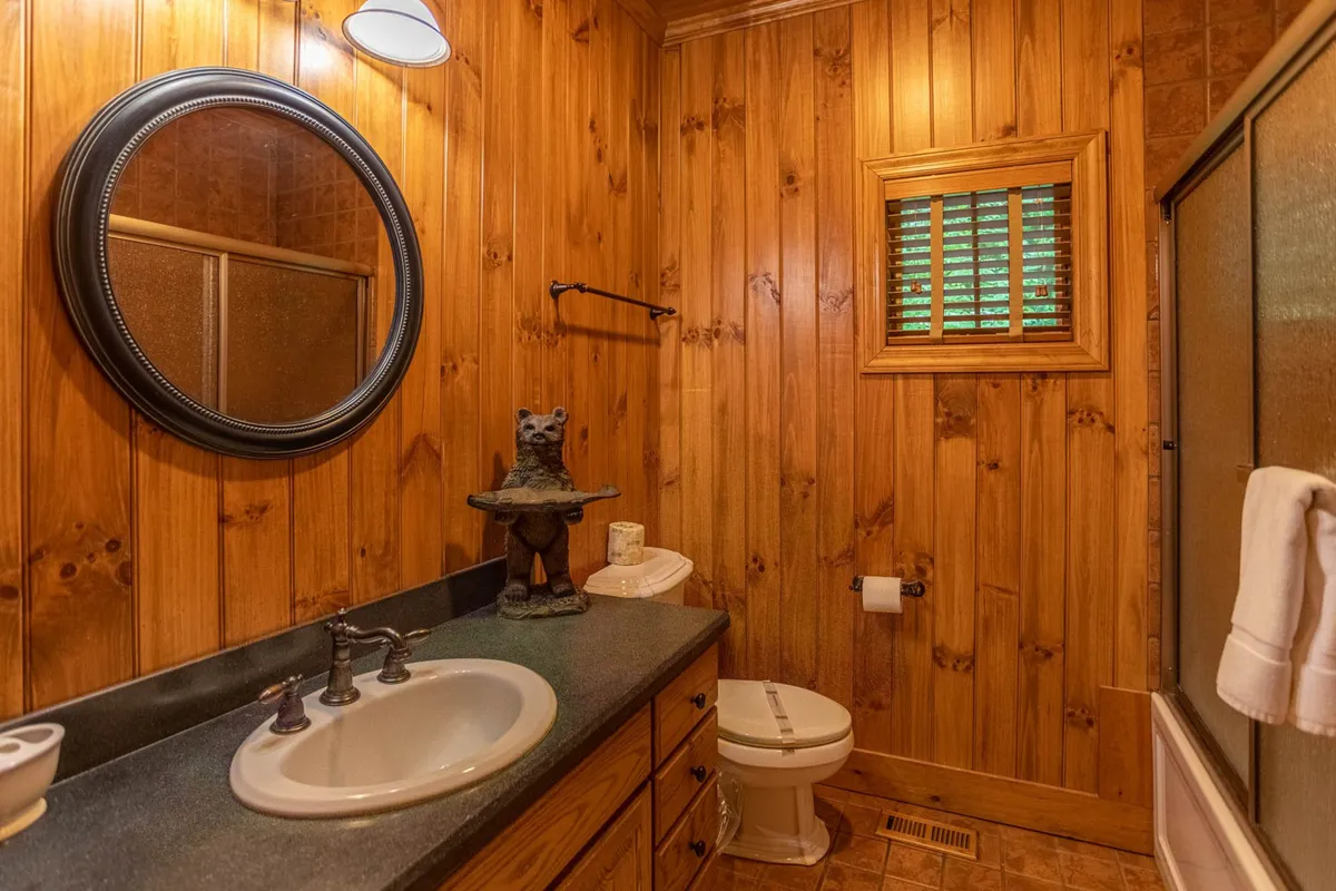 A stylish bathroom with wooden paneling, a mirror above the sink, and a bear statue adding a touch of mountain character. The mood is warm and inviting, perfect for unwinding after a day of activities.