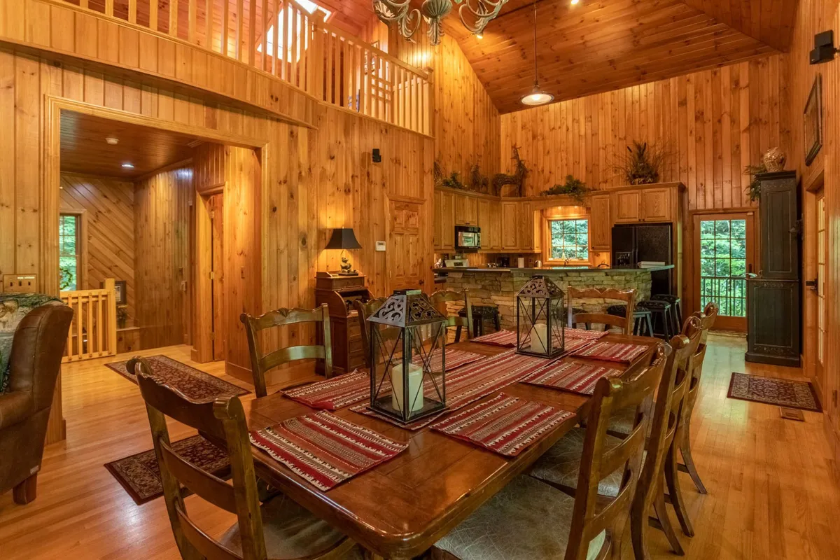 A warm, familial dining space featuring a wooden dining table set with lanterns, an open kitchen, and wood-paneled walls. The area is ideal for shared meals, celebrations, and cozy evenings spent together.
